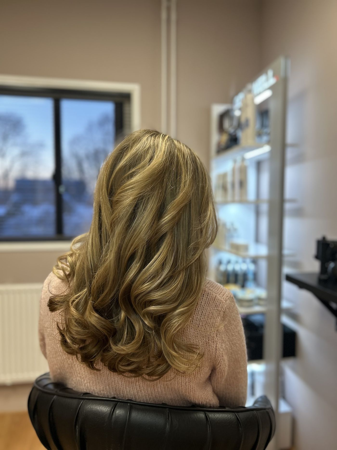 Karamelblonde krullen van achteren, klant in de salonstoel
